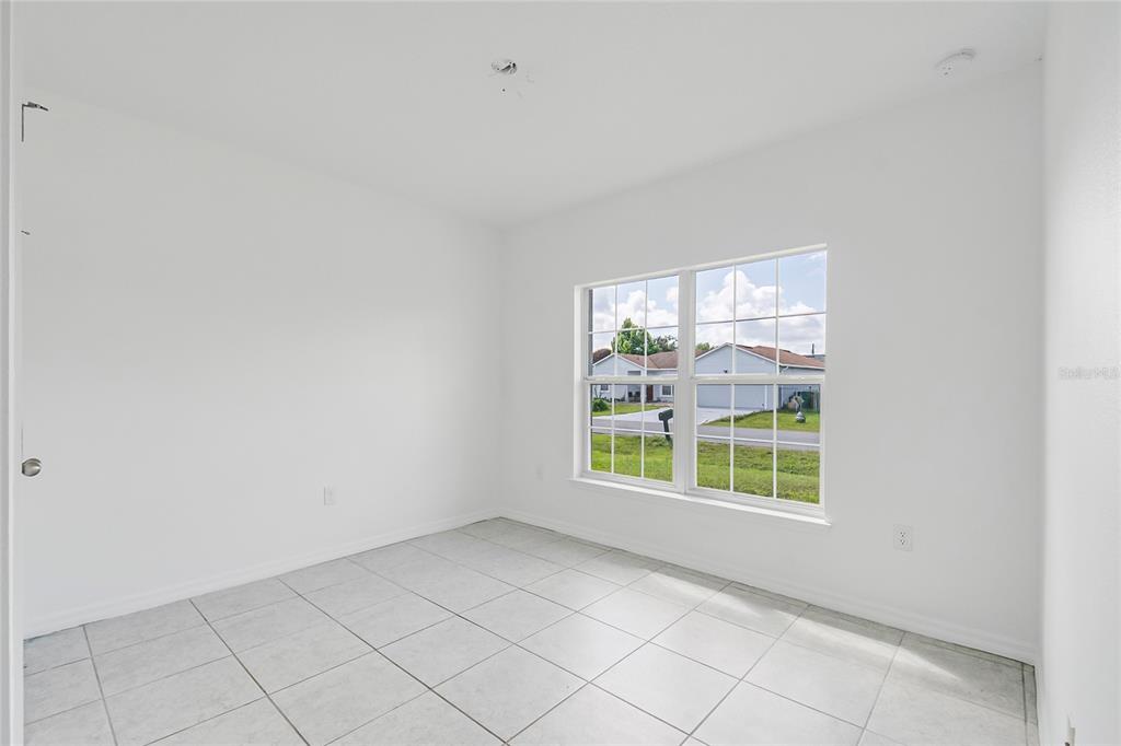 An empty room with white walls, tiled flooring, and a window overlooking a neighborhood street — 1109 MUNSTER COURT, KISSIMMEE, FL