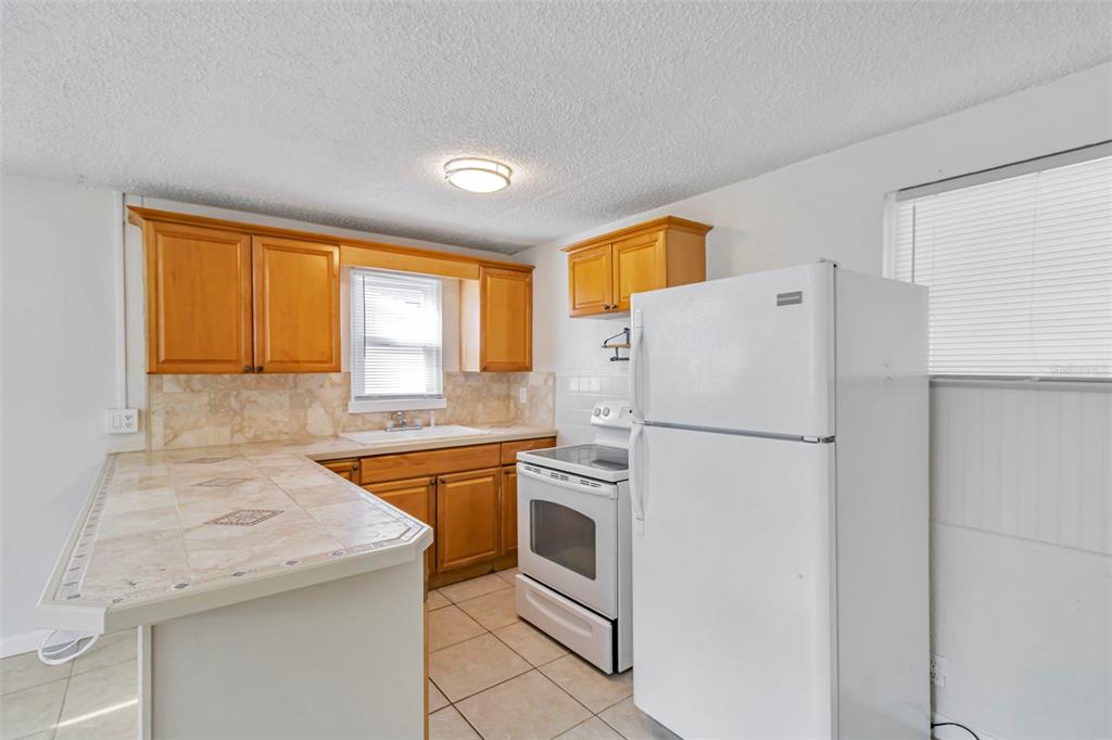 A kitchen features wood cabinets, tiled countertops, a white stove, and a white refrigerator — 809 ILLINOIS AVENUE, PALM HARBOR, FL
