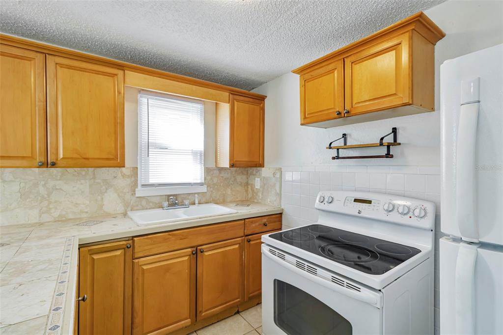 A kitchen features light wood cabinets, a white stove, a double sink, and tiled countertops — 809 ILLINOIS AVENUE, PALM HARBOR, FL