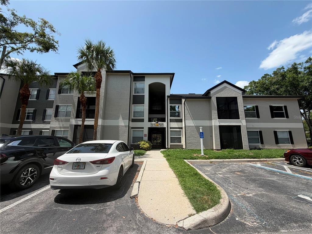 A three-story apartment building exterior with a parking lot and a white sedan in front — 7605 PISSARRO DRIVE UNIT 13106, ORLANDO, FL