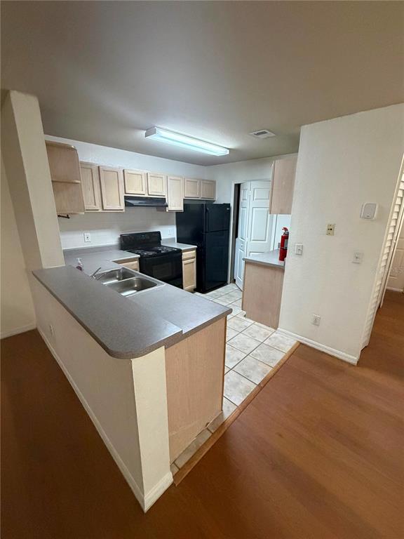 A kitchen features light wood cabinets, a black stove and refrigerator, and a breakfast bar — 7605 PISSARRO DRIVE UNIT 13106, ORLANDO, FL