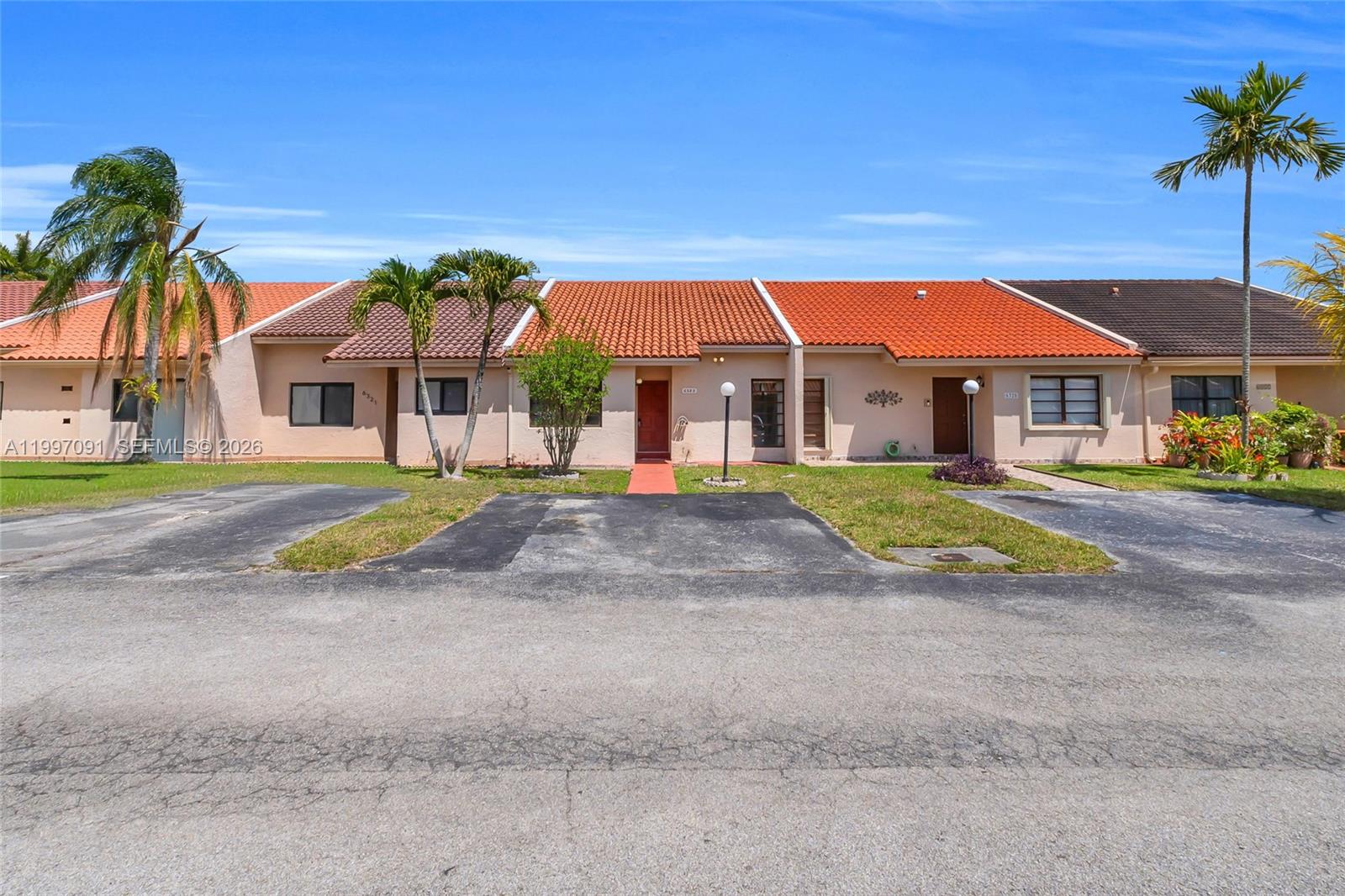 A row of single-story townhomes features terracotta-tiled roofs, beige stucco walls, and private driveways — 6323 SW 147th Place Cir, Miami FL 33193, MIAMI, FL
