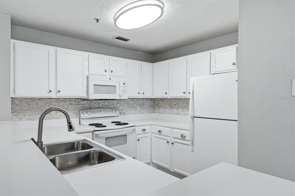 A kitchen features white cabinets, white appliances, a stone backsplash, and a double-basin sink — 4057 CROCKERS LAKE BOULEVARD UNIT 16, SARASOTA, FL
