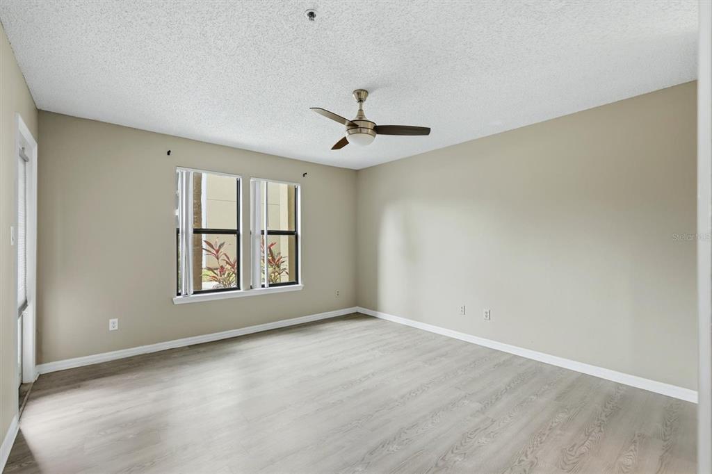 An empty room with light wood-look flooring, beige walls, a ceiling fan, and two windows — 4057 CROCKERS LAKE BOULEVARD UNIT 16, SARASOTA, FL