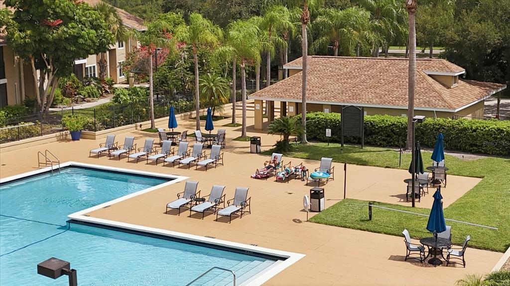 An outdoor swimming pool area with lounge chairs, tables with umbrellas, and a clubhouse building — 4057 CROCKERS LAKE BOULEVARD UNIT 16, SARASOTA, FL