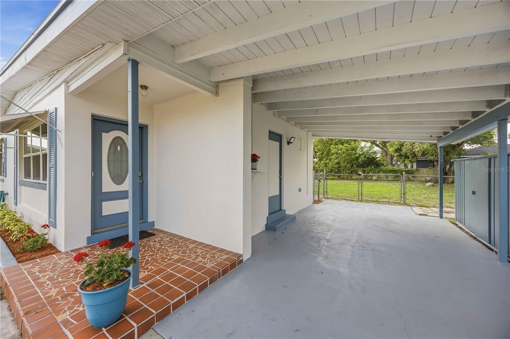 A covered carport with a concrete floor sits beside a tiled entryway and front door — 22243 HERNANDO AVENUE, PORT CHARLOTTE, FL