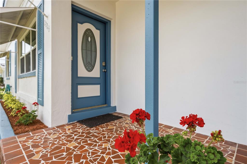 A blue front door opens onto a tiled porch with a red geranium plant — 22243 HERNANDO AVENUE, PORT CHARLOTTE, FL