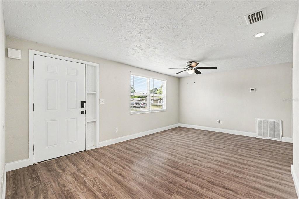 A living room features light-colored walls, wood-look flooring, a ceiling fan, and a front door — 4113 KIBLER LANE, HOLIDAY, FL
