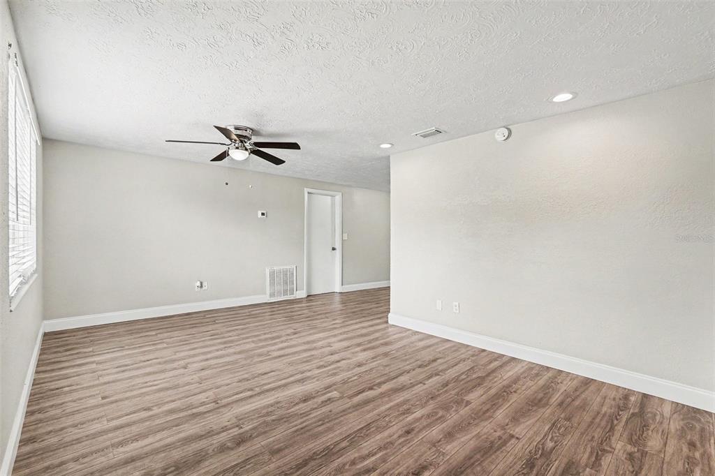 An empty room with light wood-look flooring, white walls, a ceiling fan, and a doorway — 4113 KIBLER LANE, HOLIDAY, FL