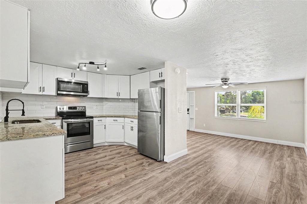 A kitchen with white cabinets and stainless steel appliances opens into a living area — 4113 KIBLER LANE, HOLIDAY, FL