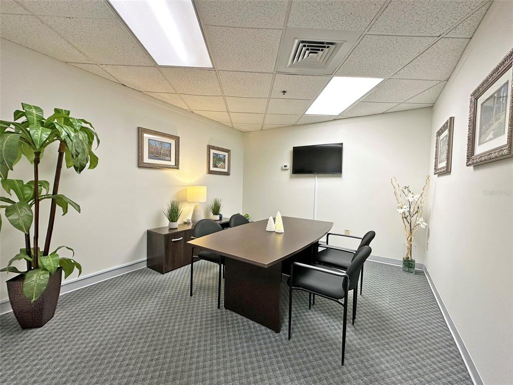 A conference room features a dark wood table, black chairs, and gray carpeted flooring — 7800 KINGSPOINTE PARKWAY UNIT 102, ORLANDO, FL