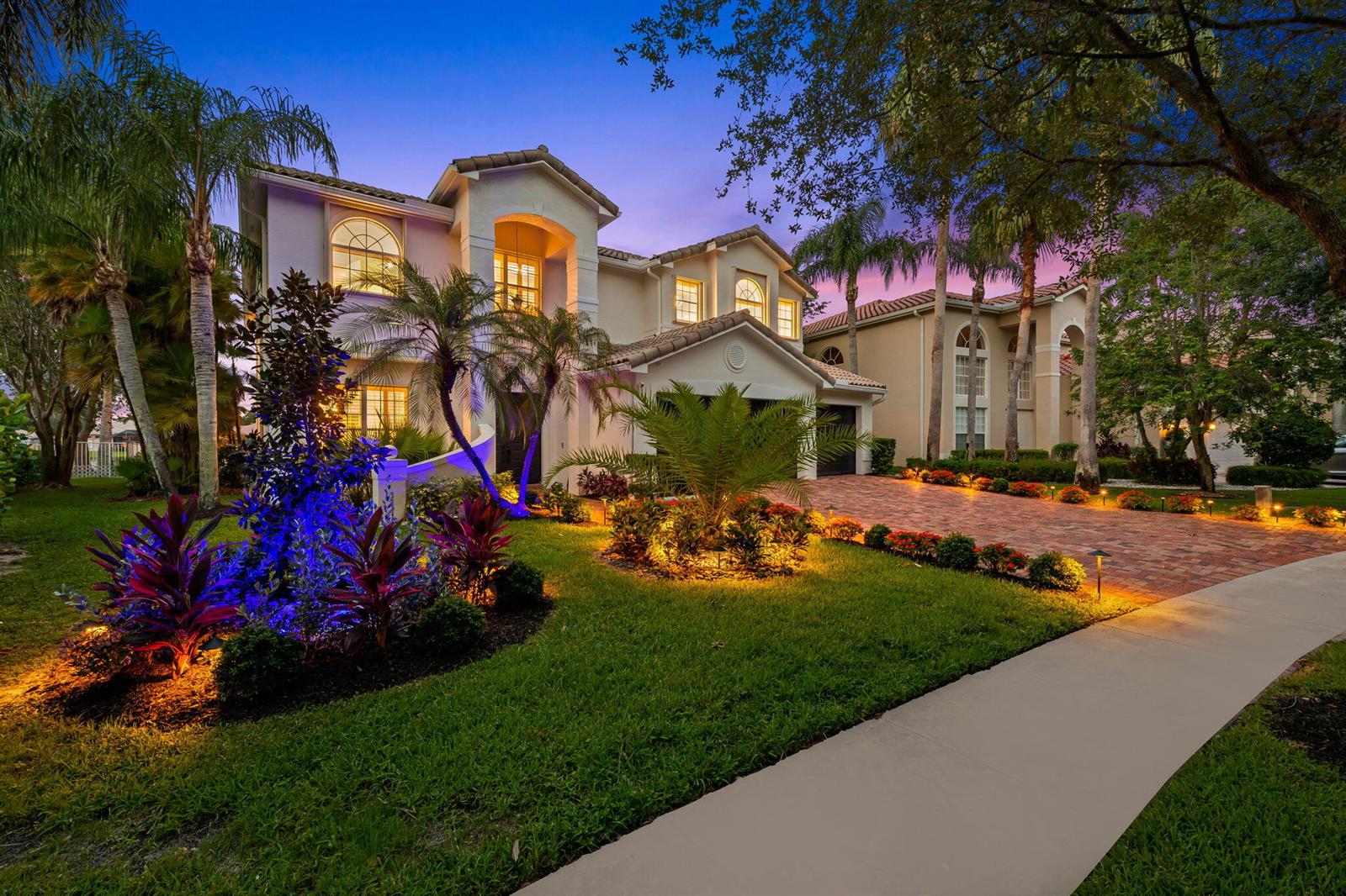 A two-story house with a brick driveway, palm trees, and landscape lighting at dusk — 9559 Barletta Winds Point, Delray Beach FL 33446, DELRAY BEACH, FL