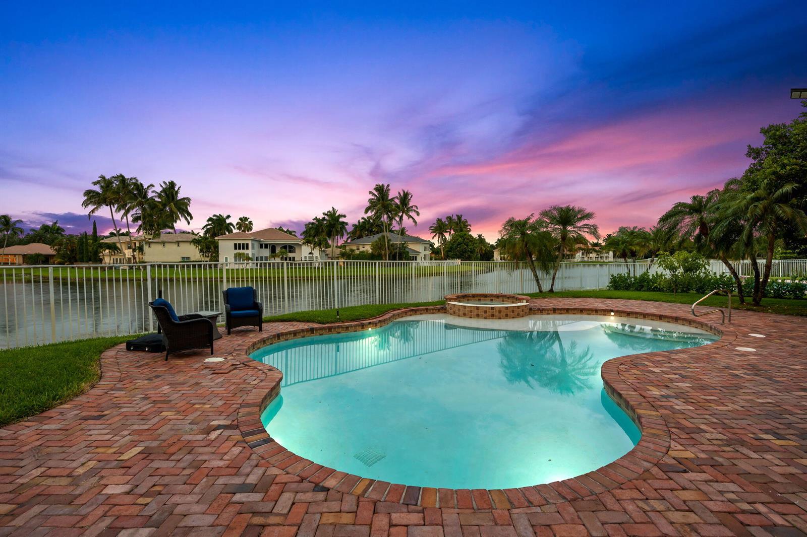 A backyard pool and hot tub overlook a lake at sunset with palm trees nearby — 9559 Barletta Winds Point, Delray Beach FL 33446, DELRAY BEACH, FL