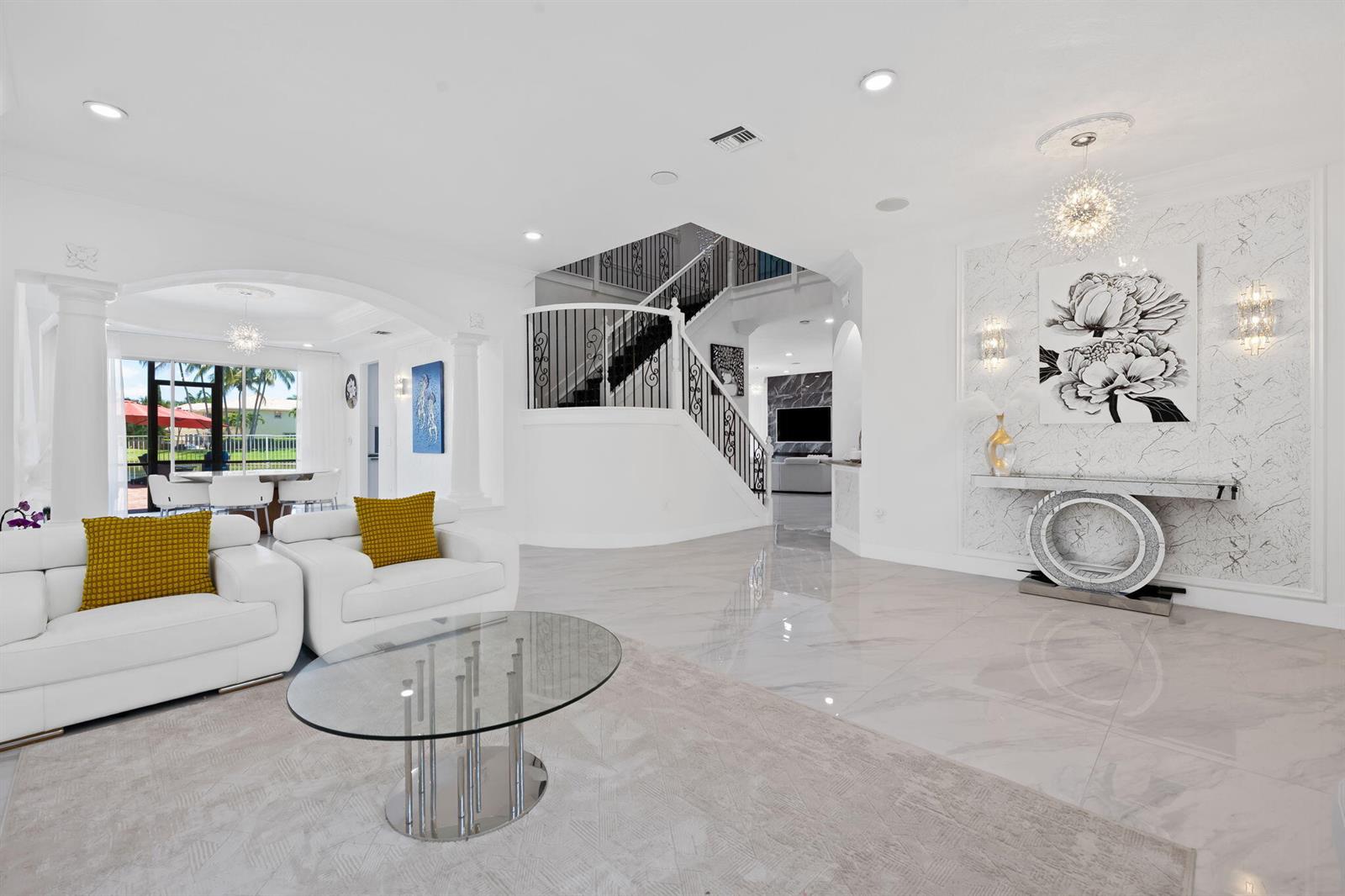A bright living room features white leather furniture, a glass coffee table, and a staircase — 9559 Barletta Winds Point, Delray Beach FL 33446, DELRAY BEACH, FL
