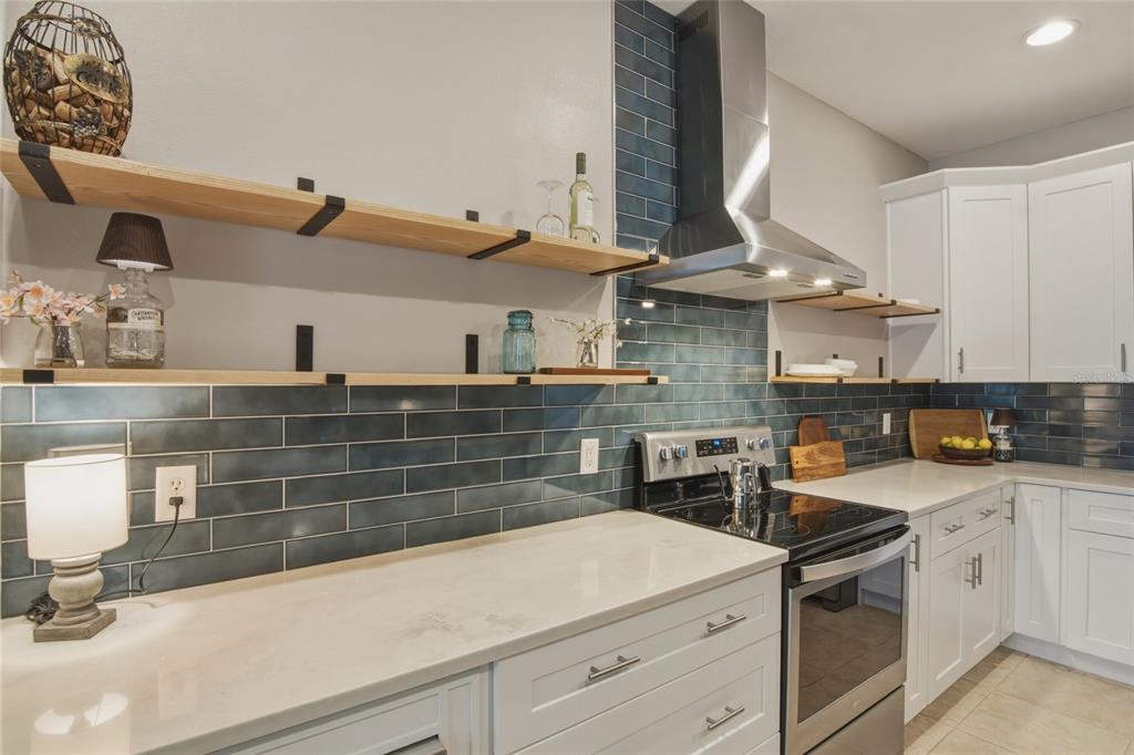 A kitchen features white cabinets, blue subway tile backsplash, open wood shelving, and stainless appliances — 1893 SANDERLING DRIVE, CLERMONT, FL
