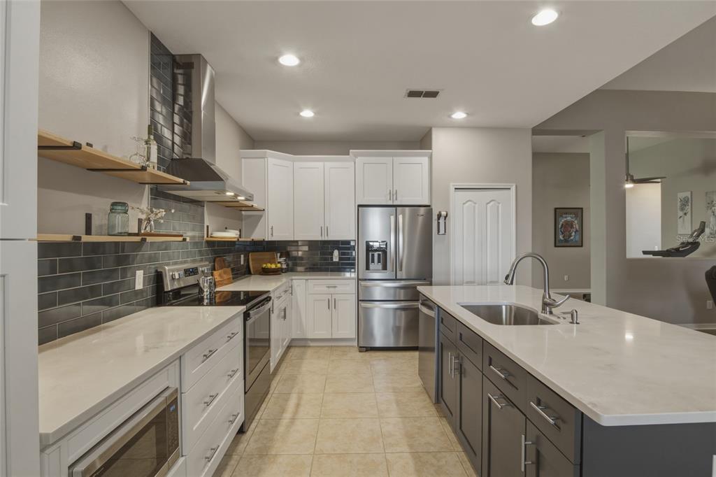 A kitchen with white upper cabinets, dark gray island cabinets, stainless appliances, and tile backsplash — 1893 SANDERLING DRIVE, CLERMONT, FL