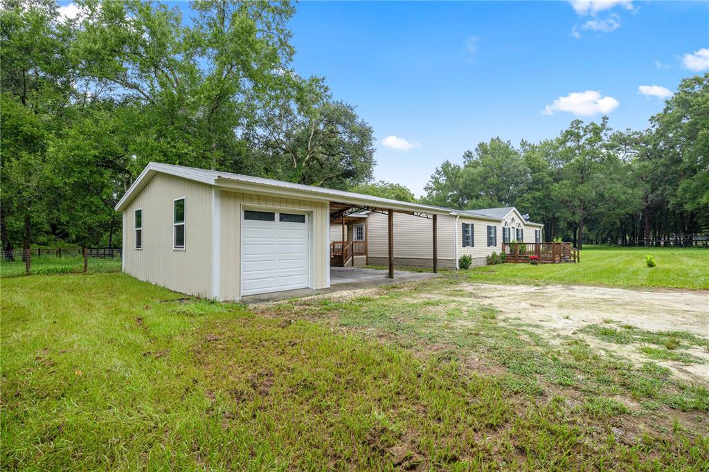 A beige detached garage with a carport attached to a single-story house on a lawn — 13250 NW 160TH AVENUE, MORRISTON, FL
