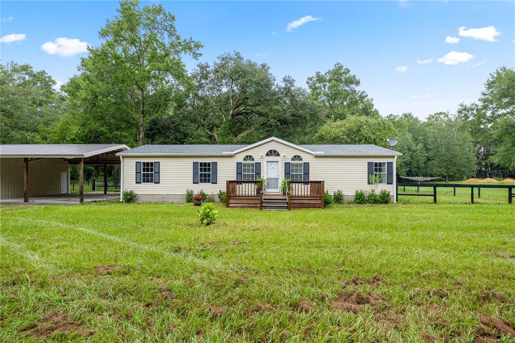 A single-story manufactured home with light siding, a front deck, and an attached metal carport — 13250 NW 160TH AVENUE, MORRISTON, FL