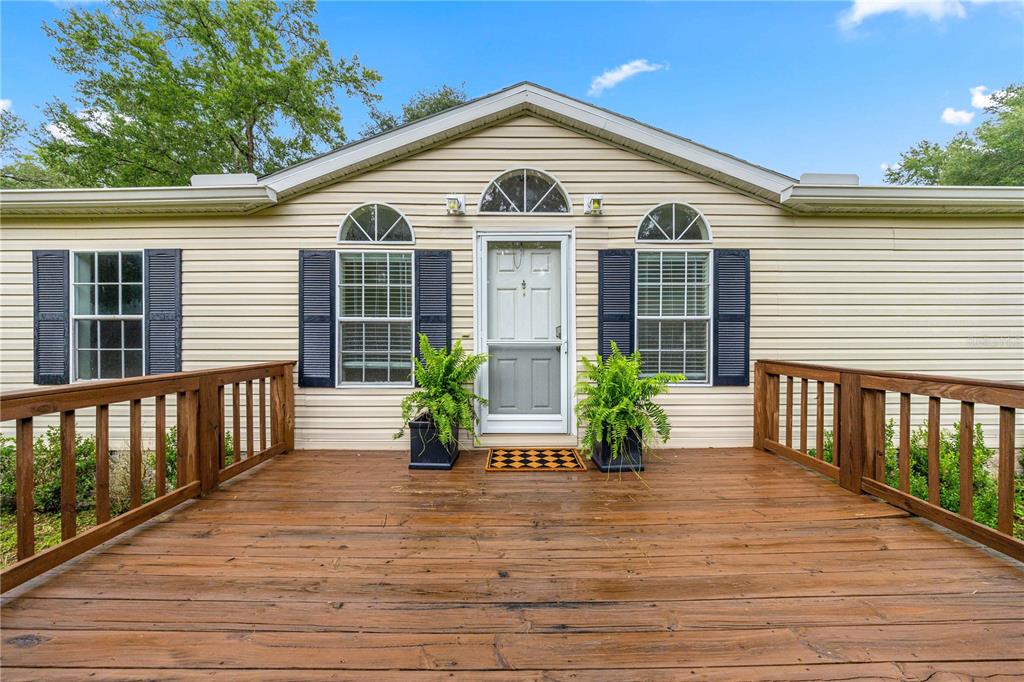 A wooden deck leads to the front entrance of a beige home with arched windows — 13250 NW 160TH AVENUE, MORRISTON, FL