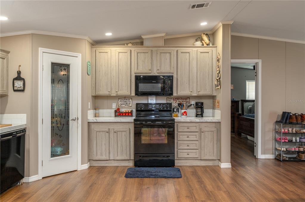 A kitchen features light wood cabinets, black appliances, and a pantry with a glass door — 15079 BRAHMA ROAD, POLK CITY, FL