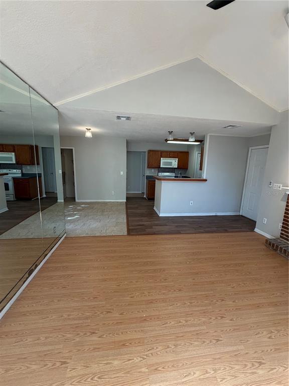 A living room with wood-look flooring, a mirrored wall, and an open kitchen beyond — 949 BIRD BAY COURT UNIT 101, LAKE MARY, FL