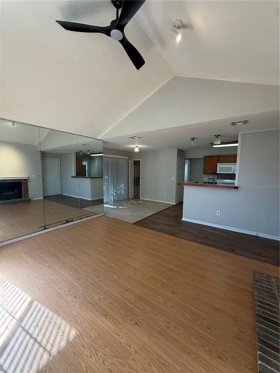A living room with wood-look flooring, a vaulted ceiling, a ceiling fan, and mirrored walls — 949 BIRD BAY COURT UNIT 101, LAKE MARY, FL