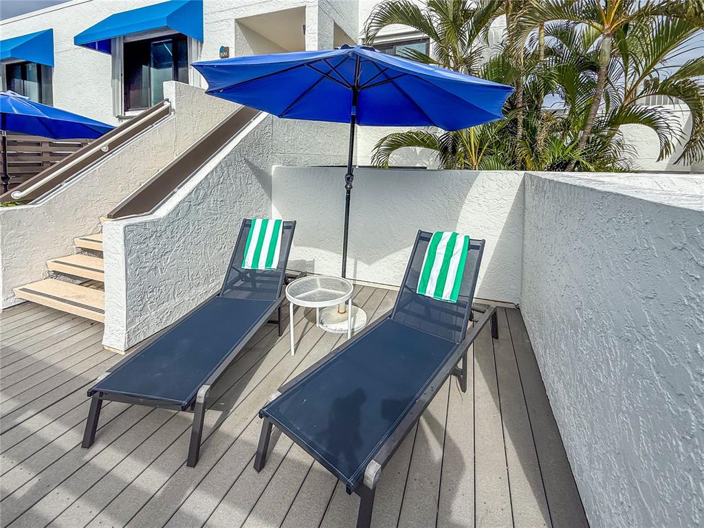 A patio features two lounge chairs with striped towels, a small table, and a blue umbrella — 829 BAYPORT WAY UNIT 829, LONGBOAT KEY, FL