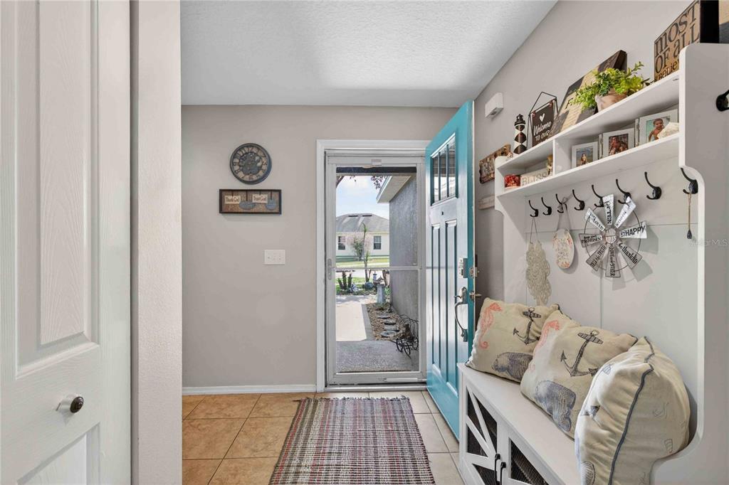 An entryway features a blue door, a white storage bench with nautical pillows, and tile flooring — 13655 LARANJA ST, CLERMONT, FL
