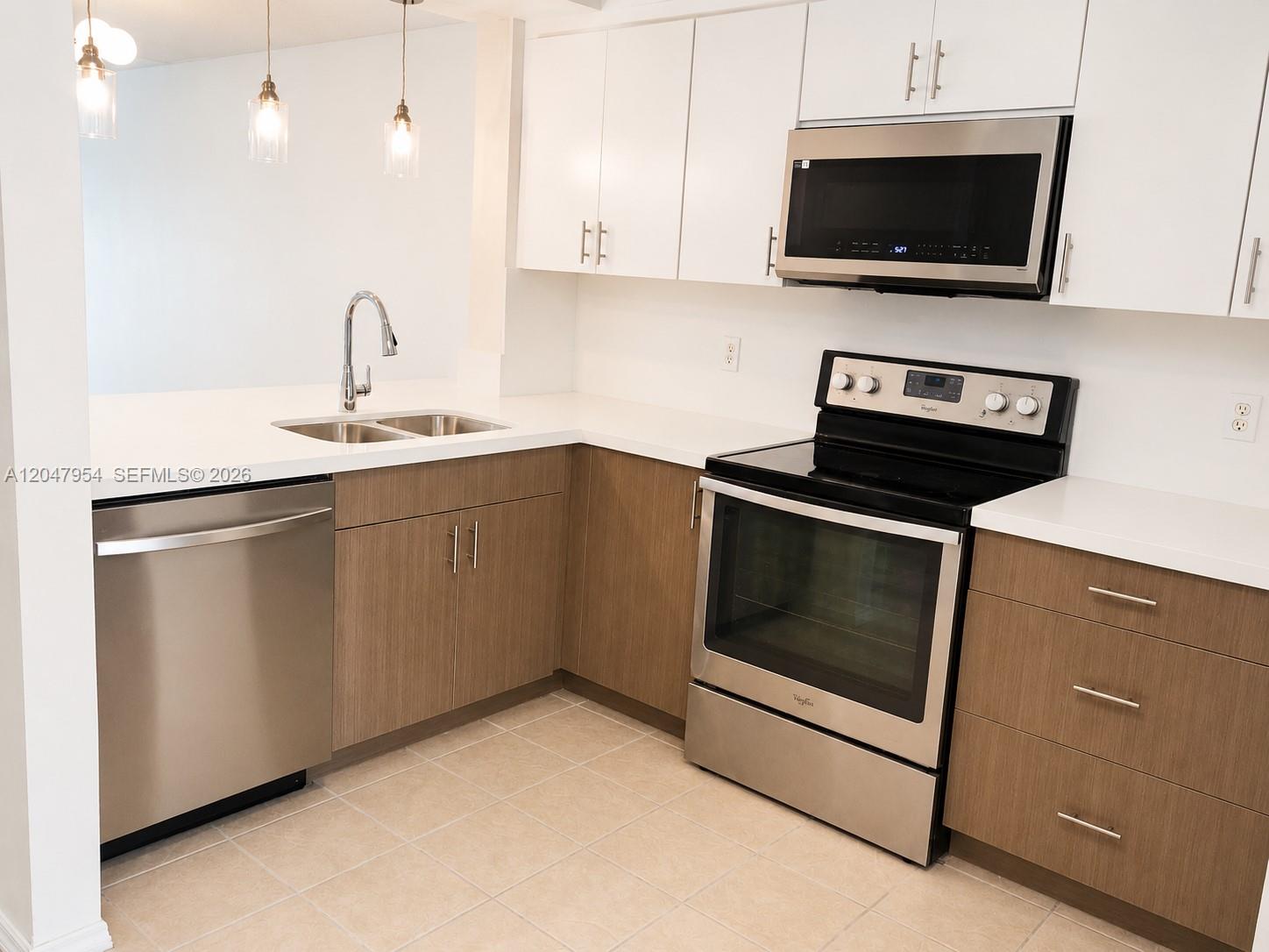 A kitchen features white upper cabinets, wood-tone lower cabinets, stainless steel appliances, and tile flooring — 3 Whitehead Cir # 3, Weston FL 33326, WESTON, FL