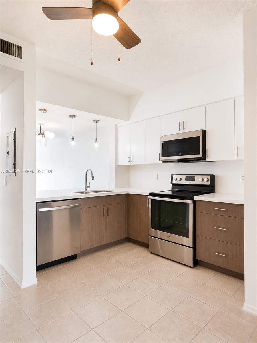 A kitchen features white upper cabinets, wood-toned lower cabinets, stainless steel appliances, and tile flooring — 3 Whitehead Cir # 3, Weston FL 33326, WESTON, FL