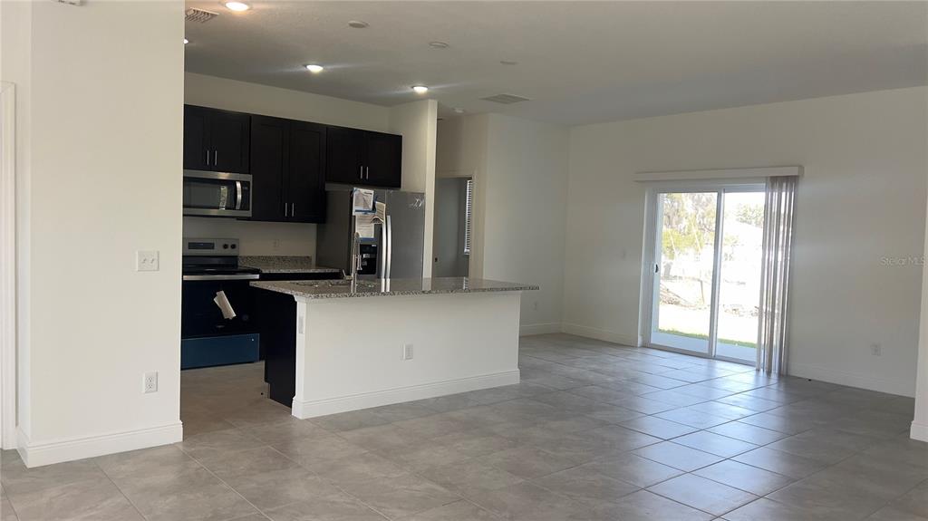 A kitchen with dark cabinets and granite countertops opens into a tiled living area — 237 CIMARRON DRIVE, POINCIANA, FL