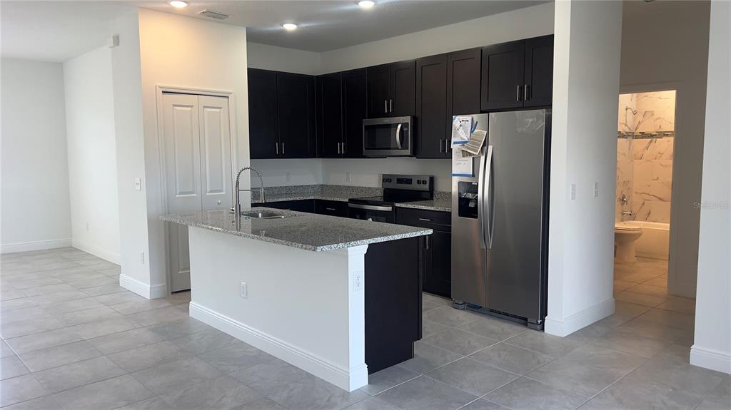 A kitchen features dark cabinets, granite countertops, stainless steel appliances, and a central island — 237 CIMARRON DRIVE, POINCIANA, FL
