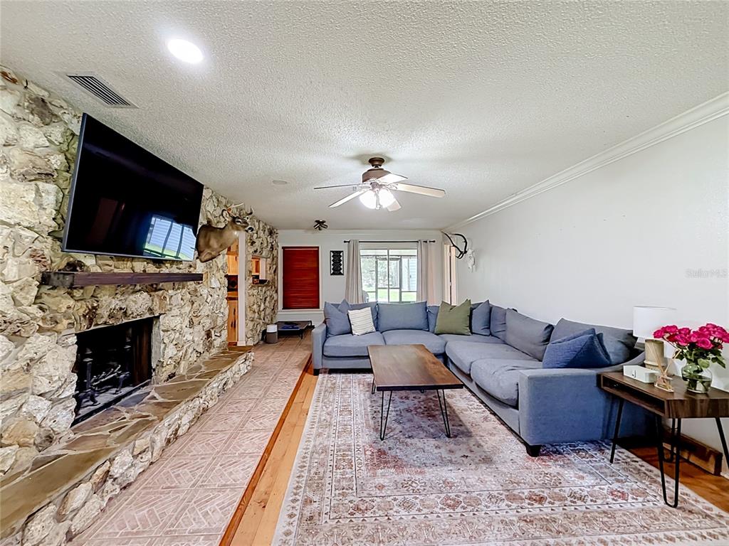 A living room features a stone fireplace, a large sectional sofa, and a ceiling fan — 26586 SE HIGHWAY 42, UMATILLA, FL