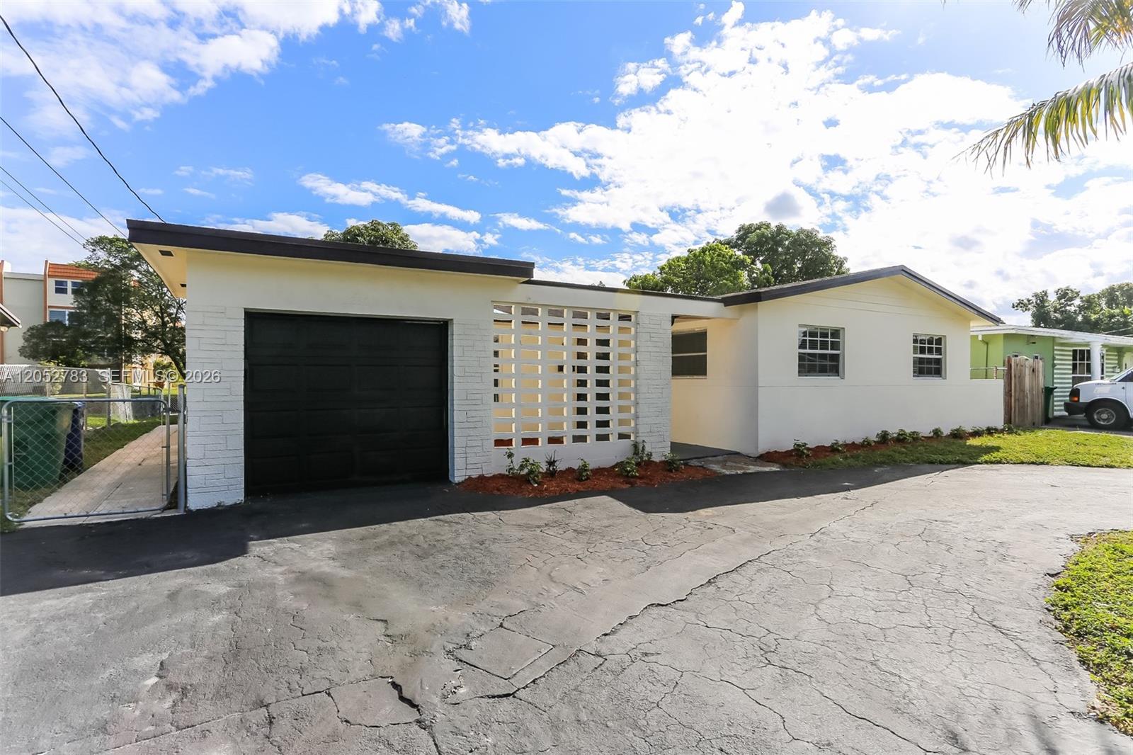 A white single-story house features a black garage door and a decorative breeze block wall — 2230 NW 42nd Ave, Lauderhill FL 33313, LAUDERHILL, FL