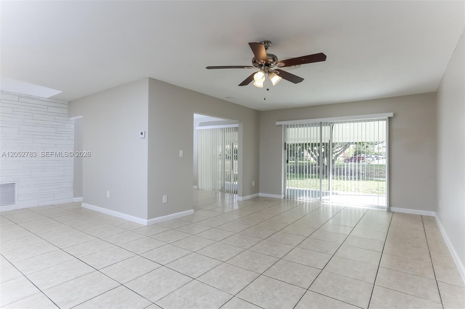 An empty living room features light-colored tile flooring, a ceiling fan, and sliding glass doors — 2230 NW 42nd Ave, Lauderhill FL 33313, LAUDERHILL, FL