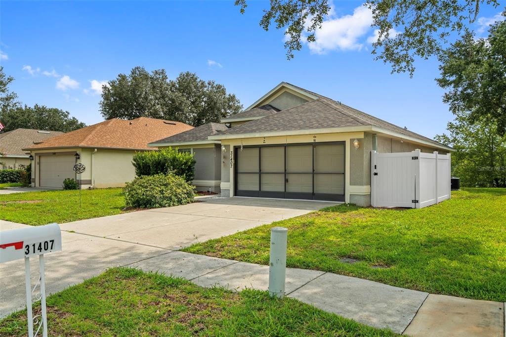 A single-story house with a two-car garage and a white vinyl fence — 31407 SATINLEAF RUN, BROOKSVILLE, FL