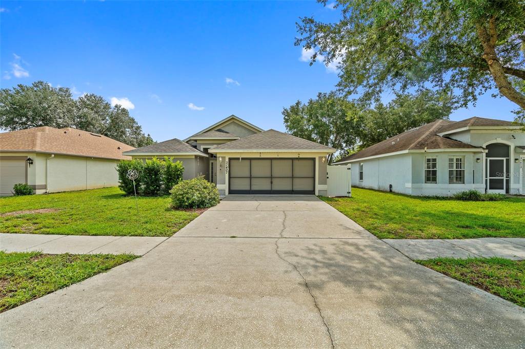 A single-story house with a two-car garage and a concrete driveway under a blue sky — 31407 SATINLEAF RUN, BROOKSVILLE, FL