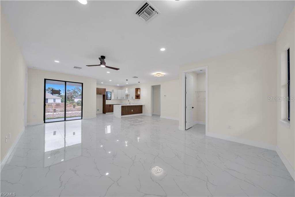 An open-concept living area features white marble-look tile flooring, a kitchen island, and sliding doors — 2901 VILLA AVENUE S, LEHIGH ACRES, FL