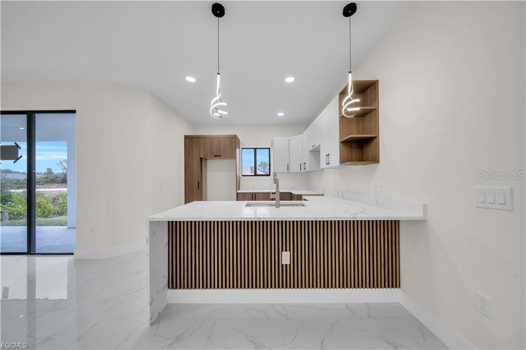 A modern kitchen features a marble-topped island with wood-slat detailing and white cabinetry — 2901 VILLA AVENUE S, LEHIGH ACRES, FL