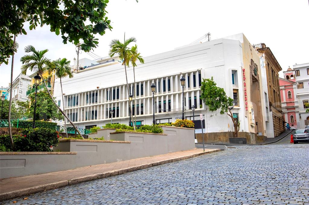 A white multi-story building with vertical window fins sits on a cobblestone street corner — 203 RECINTO SUR UNIT 5, OLD SAN JUAN, PR