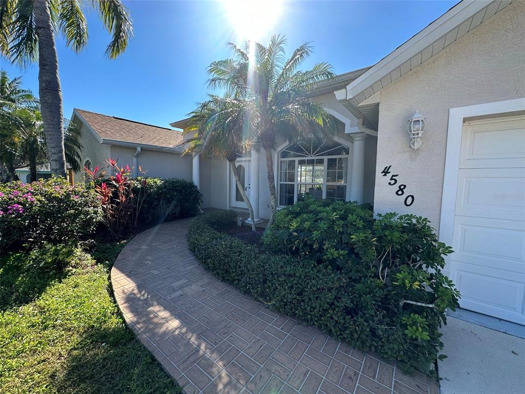A paved walkway leads to the front entrance of a house with a palm tree — 4580 CRYSTAL ROAD, VENICE, FL
