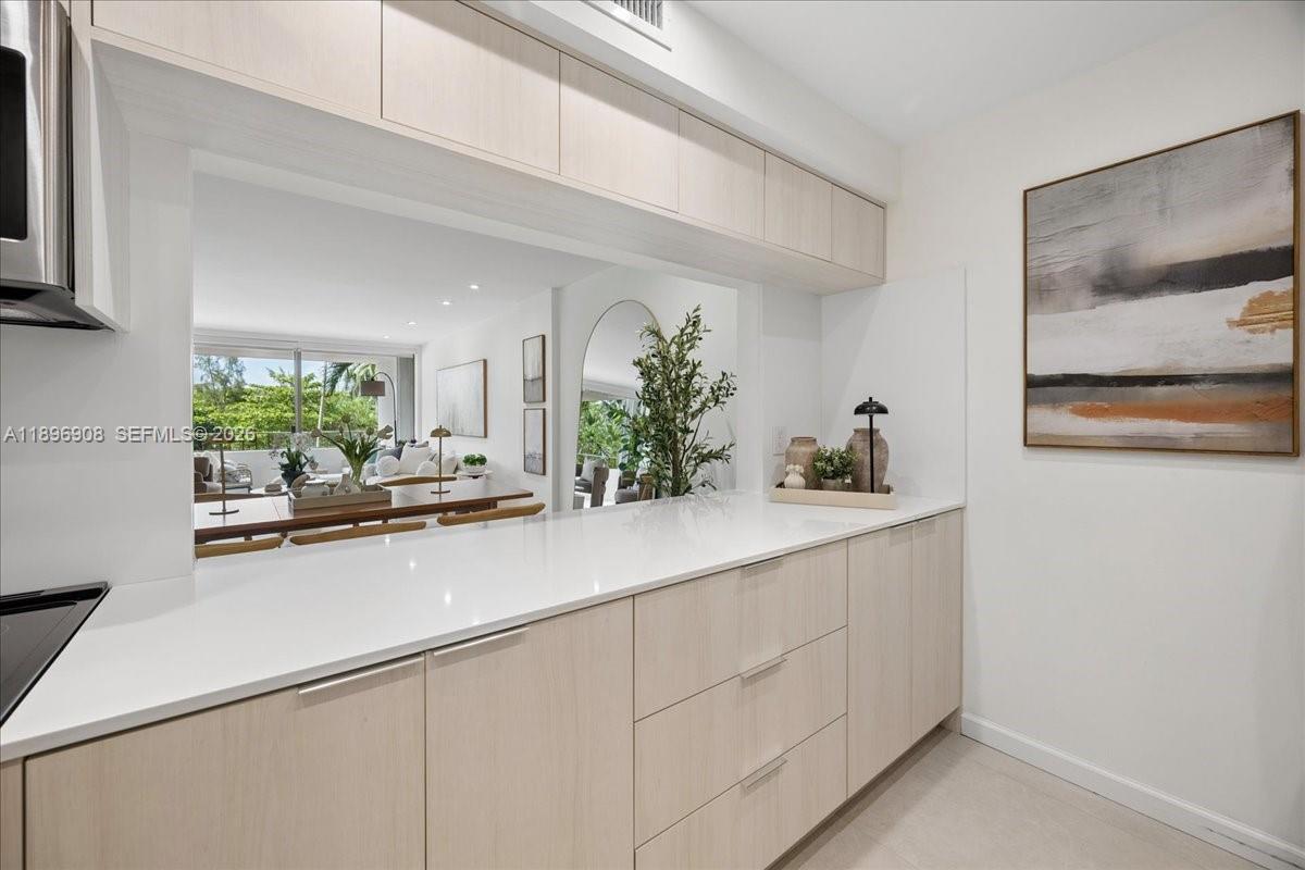 A kitchen features light wood cabinets, white countertops, and a pass-through window to the living area — 155 Ocean Lane Dr # 302, Key Biscayne FL 33149, KEY BISCAYNE, FL