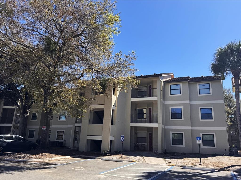A three-story apartment building features beige stucco walls, balconies, and a paved parking lot — 3028 PARKWAY BOULEVARD UNIT 210, KISSIMMEE, FL