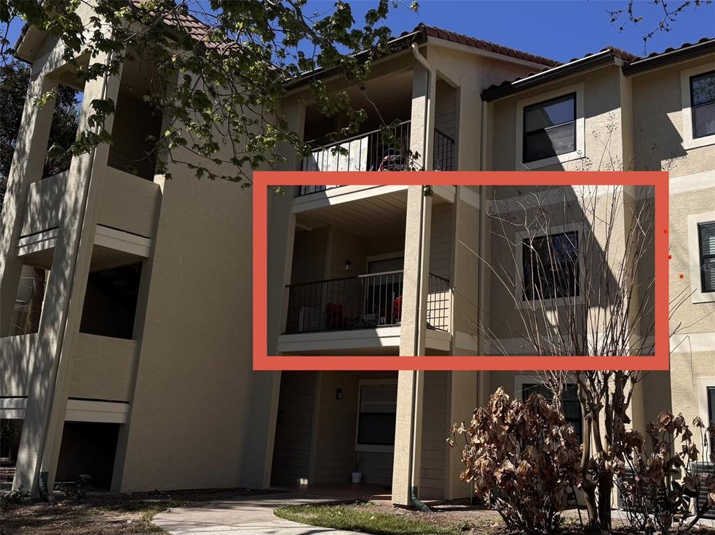 A multi-story apartment building exterior featuring a second-floor balcony enclosed within a red frame — 3028 PARKWAY BOULEVARD UNIT 210, KISSIMMEE, FL
