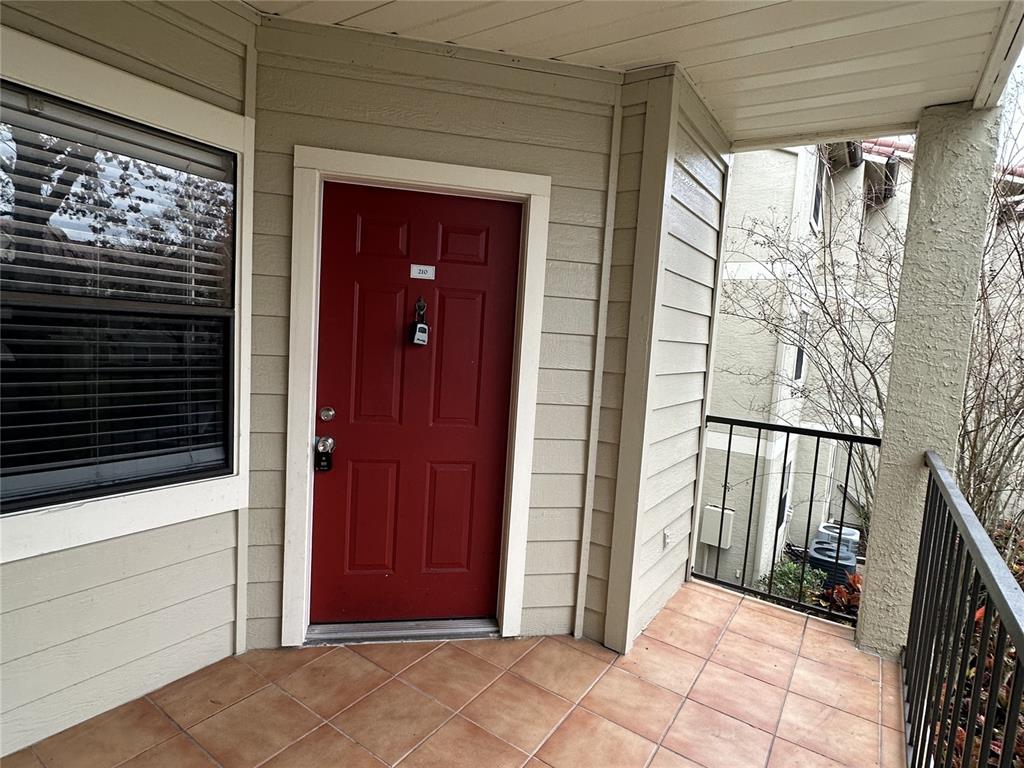 A red front door with a lockbox sits on a tiled balcony with metal railings — 3028 PARKWAY BOULEVARD UNIT 210, KISSIMMEE, FL