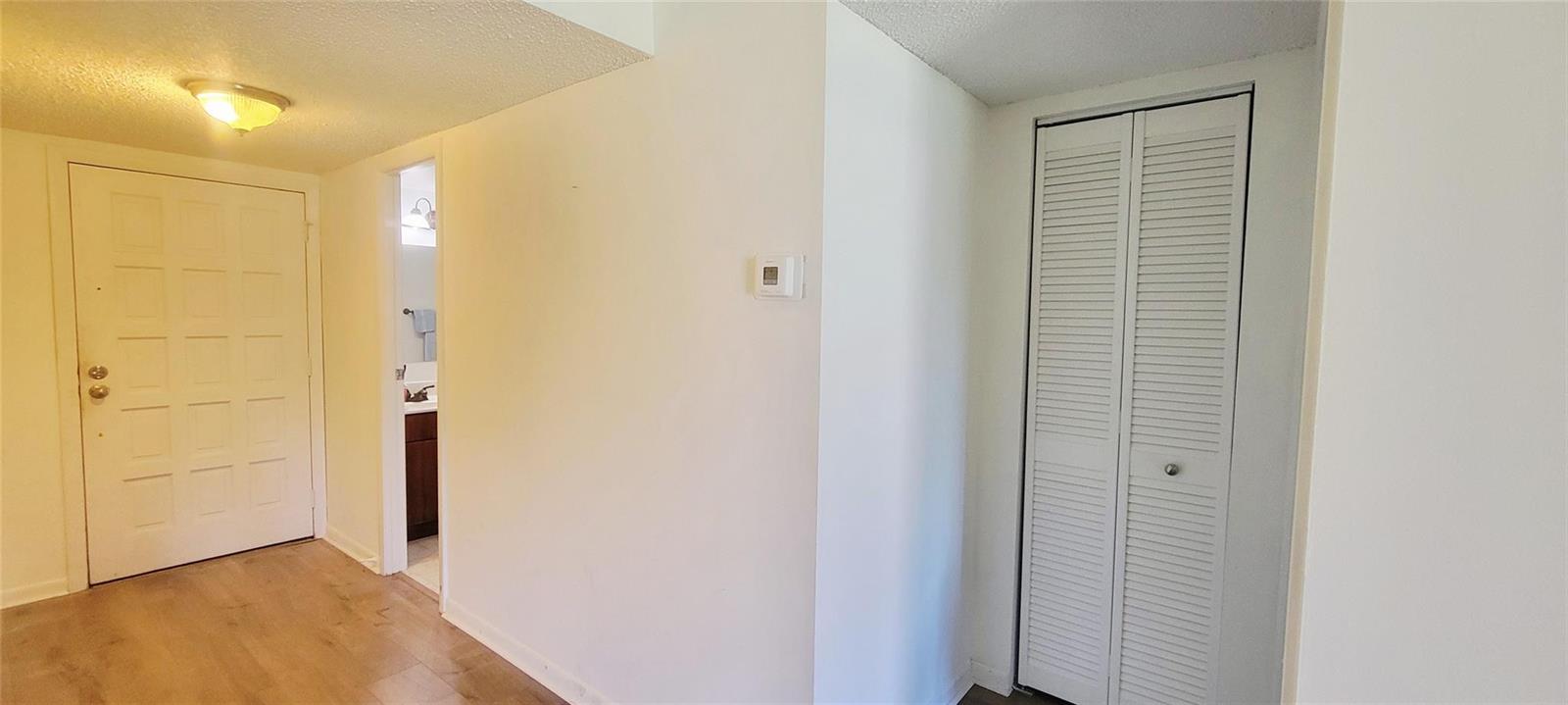A hallway features wood-look flooring, a white door, a closet with louvered doors, and a thermostat — 6260 S Falls Circle Drive # 206, Lauderhill FL 33319, LAUDERHILL, FL