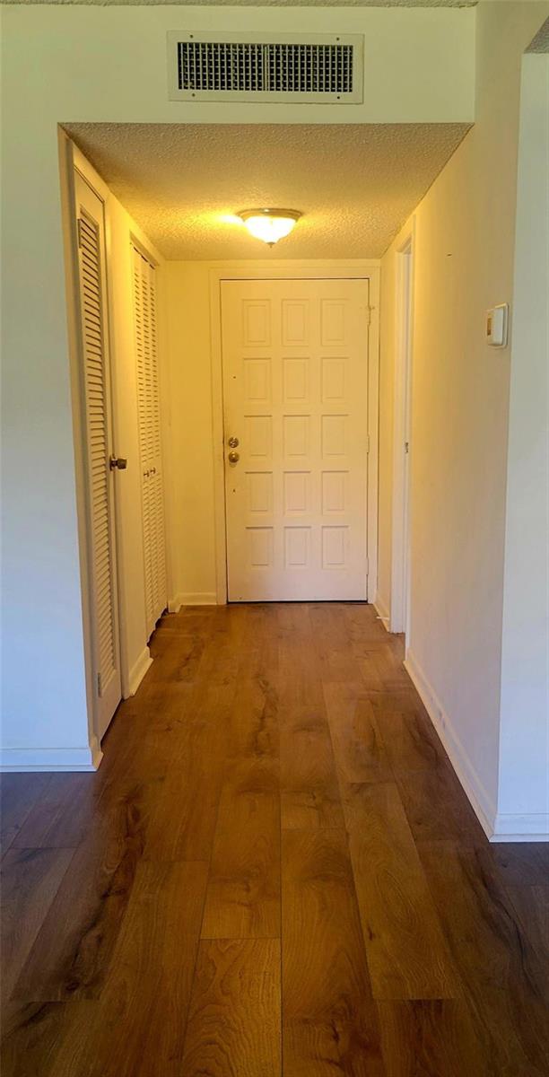 A hallway with wood-look flooring leads to a white front door and a louvered closet — 6260 S Falls Circle Drive # 206, Lauderhill FL 33319, LAUDERHILL, FL