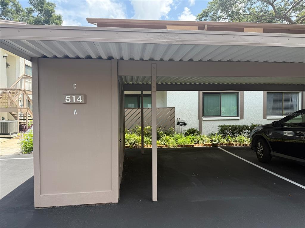 A covered parking carport with a numbered sign and a parked vehicle — 514 LONGFELLOW COURT UNIT C, SAFETY HARBOR, FL