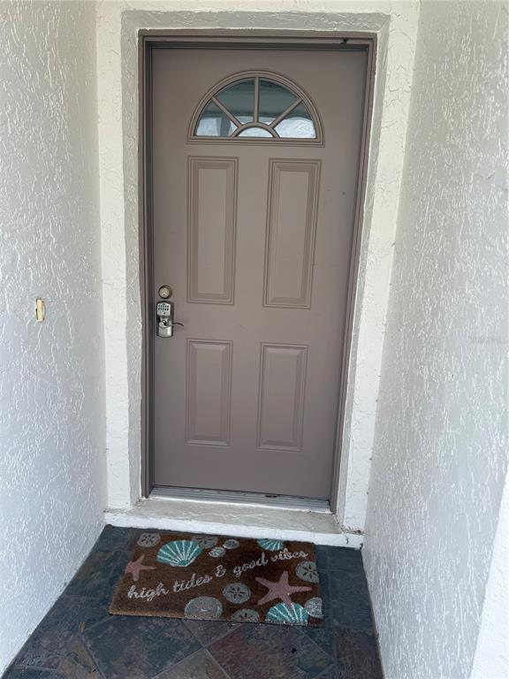 A brown front door with a semi-circular window sits above a decorative seashell doormat — 514 LONGFELLOW COURT UNIT C, SAFETY HARBOR, FL