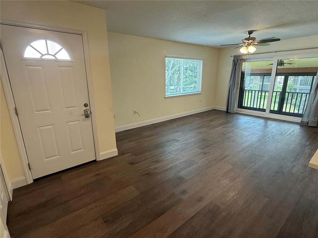 An empty living room features dark wood-look flooring, a ceiling fan, and a glass sliding door — 514 LONGFELLOW COURT UNIT C, SAFETY HARBOR, FL